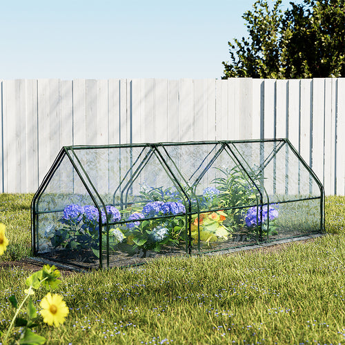 Small greenhouse with plants on a grassy area with a wooden fence in the background