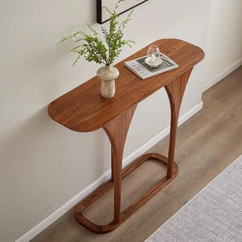 Wooden console table with a plant and decorative items against a white wall.