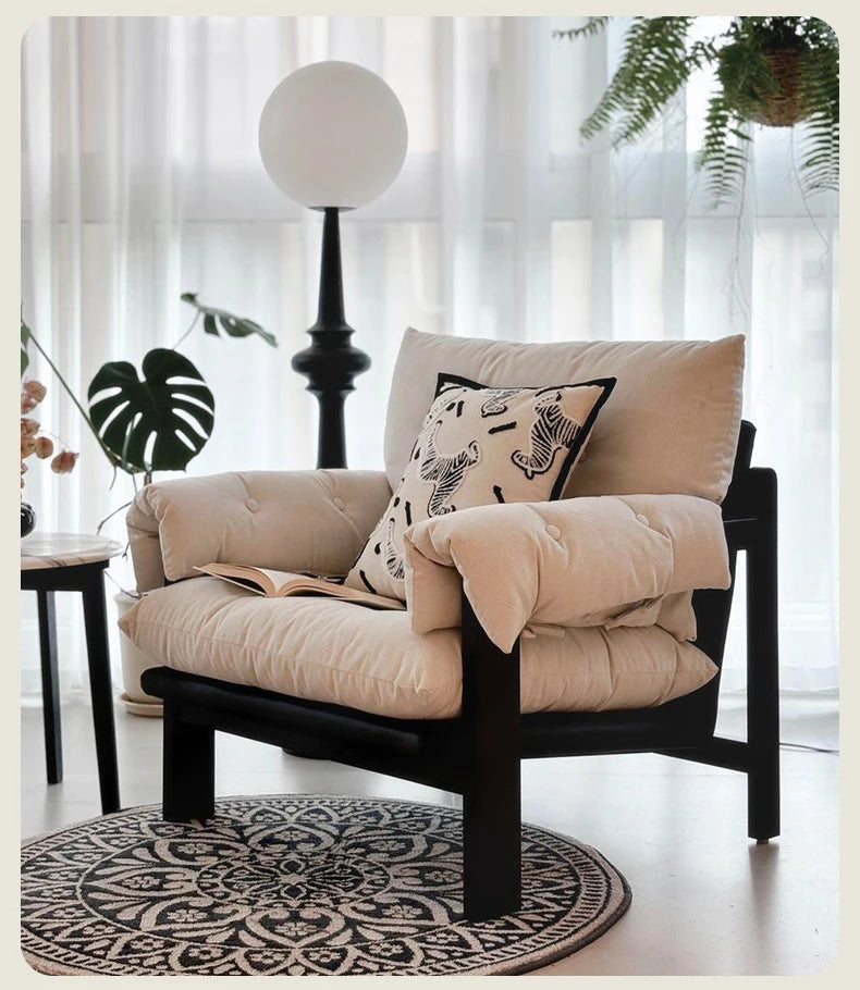 Beige armchair with cushions and a blanket in a bright room with curtains and plants.