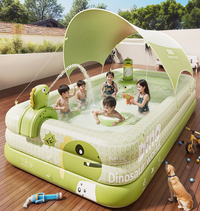 Children playing in a dinosaur-themed inflatable pool on a wooden deck with a dog nearby.