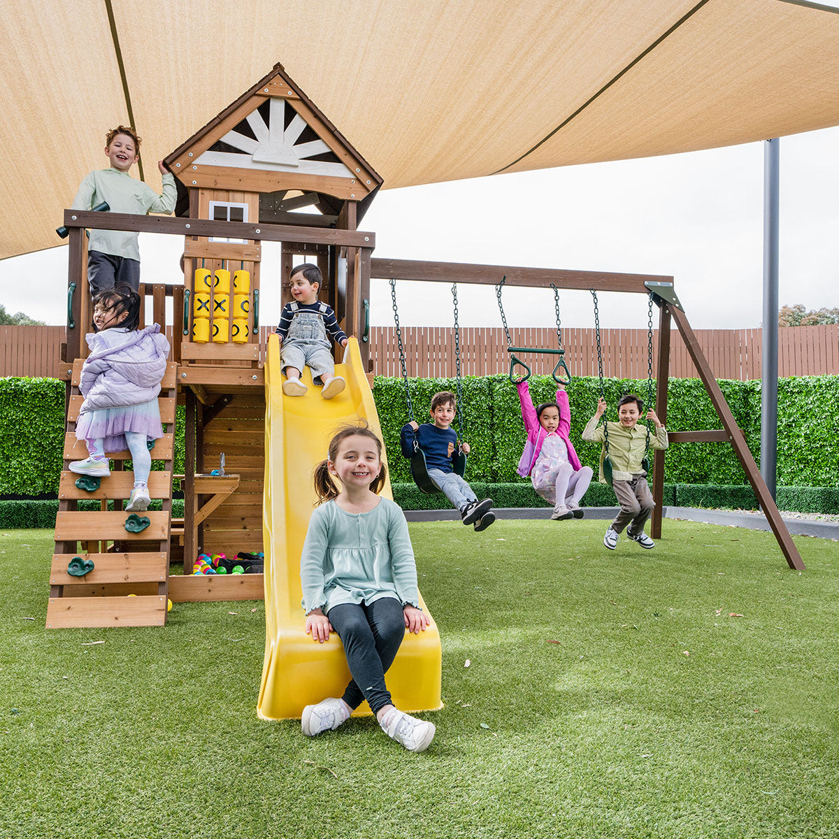 Children playing on a wooden playground set with slides and swings.