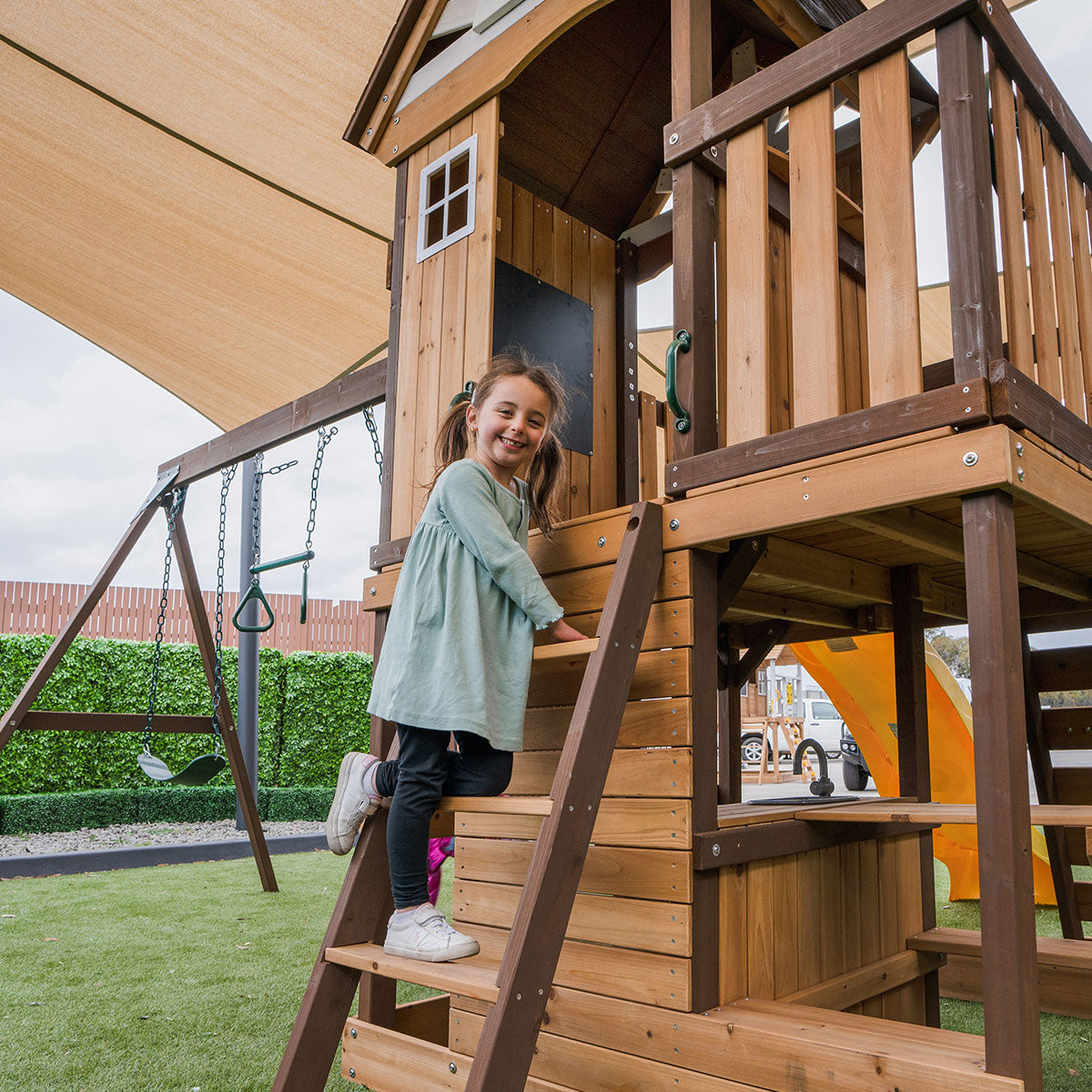 Child climbing a wooden playhouse with playground equipment in the background