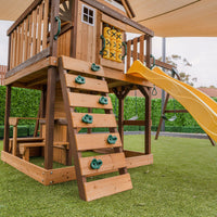 Wooden playset with a yellow slide on a grassy area