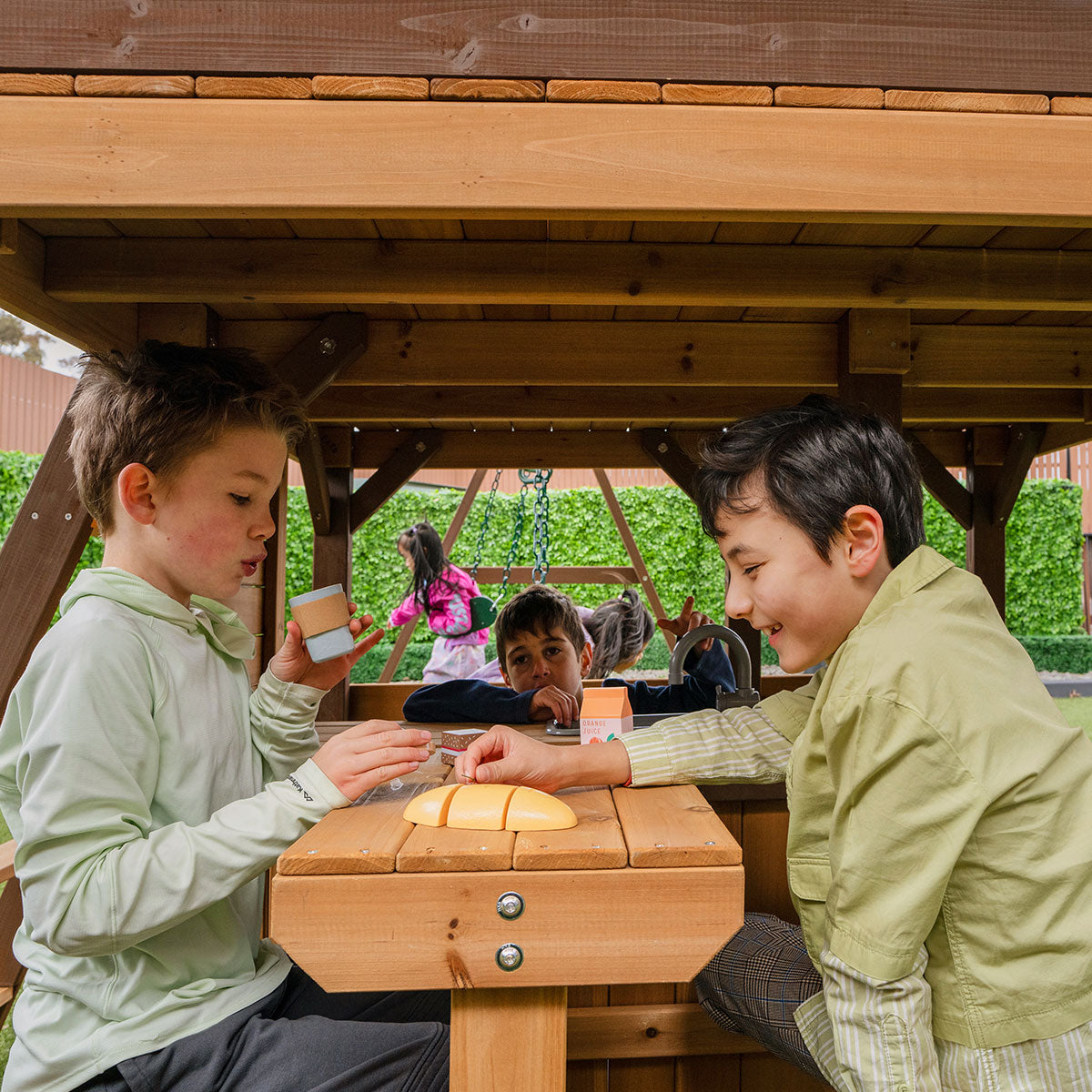 Two children playing with a wooden toy under a wooden structure.