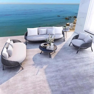 Outdoor patio set with white cushions and a coffee table on a deck overlooking the ocean.