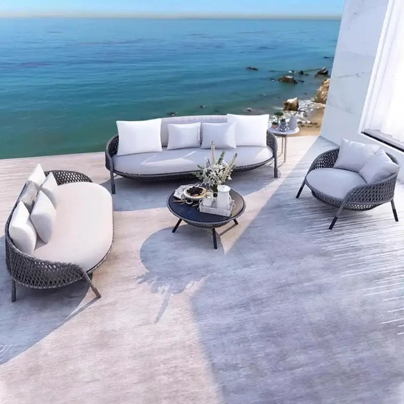Outdoor patio set with white cushions and a coffee table on a deck overlooking the ocean.