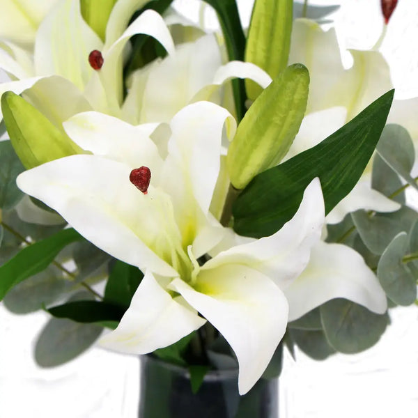 Artificial white lily in glass vase with green leaves