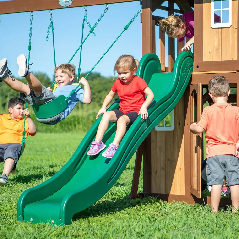 Children playing on a green slide in backyard discovery lakewood play centre with raised fort and real door