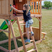Young girl climbing on wooden playhouse in backyard discovery montpelier play centre set, featuring monkey bars and super speedy slide
