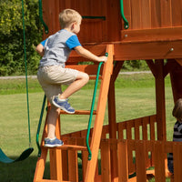 Young boy climbing on a wooden swing set at backyard discovery skyfort ii play centre