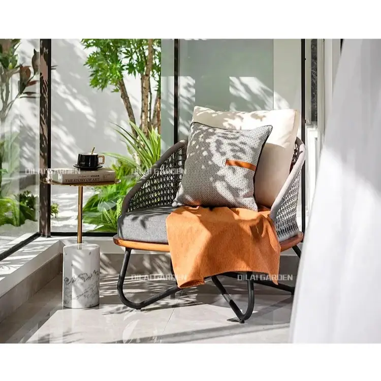 Modern outdoor chair with cushions and a small table on a patio with plants and sunlight.